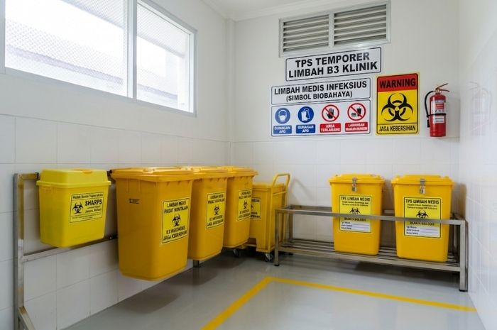 Tempat penyimpanan sementara limbah B3 di klinik dengan wadah limbah medis dan benda tajam yang dipisahkan.